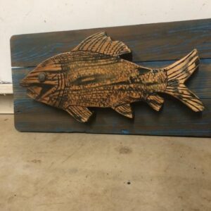 A fish carved out of wood on top of a wooden board.